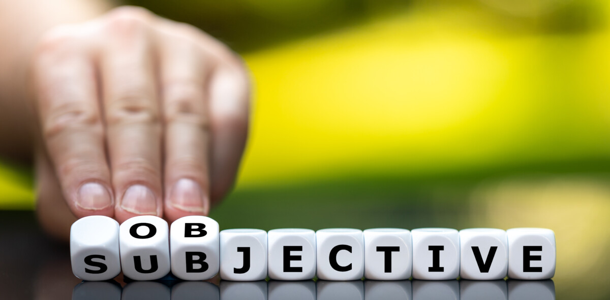 Une main humaine fait pivoter des dés affichant les lettres du mot "subjective", pour les transformer en "objective", ou inversement. L'image illustre le passage entre subjectivité et objectivité, symbolisant le choix ou la perception dans une situation, notamment en contexte d’analyse ou de résolution de conflit.
