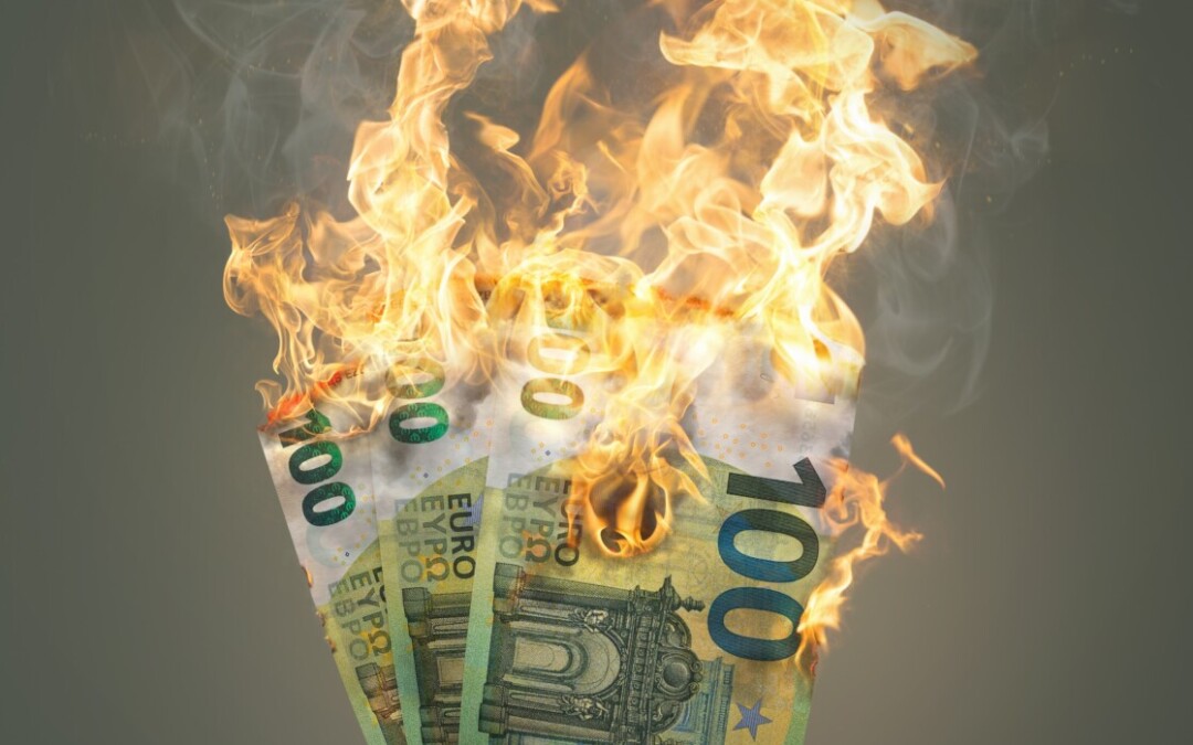 "Une main tient plusieurs billets de 100 euros en feu, symbolisant la perte d'argent, le gaspillage de ressources financières ou une crise économique."
