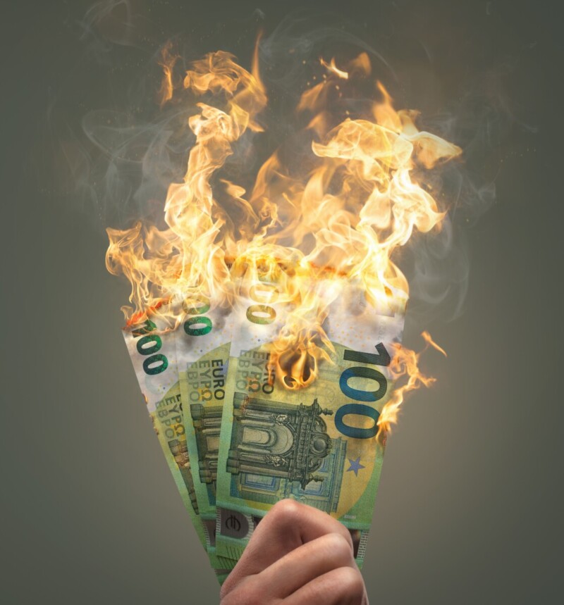 "Une main tient plusieurs billets de 100 euros en feu, symbolisant la perte d'argent, le gaspillage de ressources financières ou une crise économique."