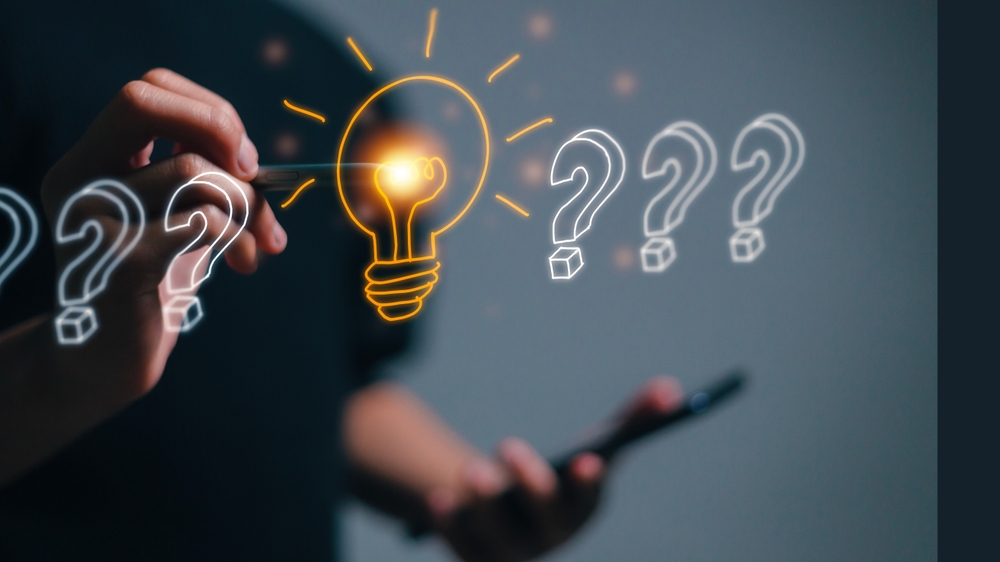 Une personne tient un smartphone dans une main et utilise un stylet pour dessiner ou interagir avec une série d’éléments visuels en réalité augmentée ou virtuelle. Plusieurs points d’interrogation blancs apparaissent en ligne, et au centre, une ampoule lumineuse orange symbolise une idée ou une solution. L’image illustre le passage de la question à la réponse, ou le processus de résolution de problème par l'innovation ou la réflexion créative.