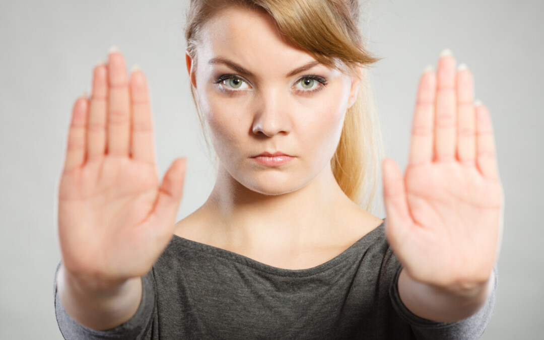 Une femme regarde fixement l’objectif, les bras tendus devant elle avec les paumes ouvertes en signe d’opposition ou de mise à distance. Cette posture symbolique évoque une volonté ferme de poser des limites, typique d’une situation de conflit en entreprise où l’affirmation de soi devient nécessaire pour se protéger ou défendre ses droits face à une tension interpersonnelle ou organisationnelle.