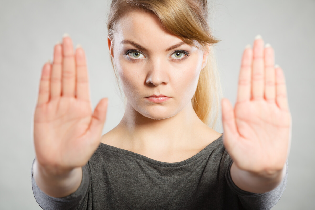 Une femme regarde fixement l’objectif, les bras tendus devant elle avec les paumes ouvertes en signe d’opposition ou de mise à distance. Cette posture symbolique évoque une volonté ferme de poser des limites, typique d’une situation de conflit en entreprise où l’affirmation de soi devient nécessaire pour se protéger ou défendre ses droits face à une tension interpersonnelle ou organisationnelle.