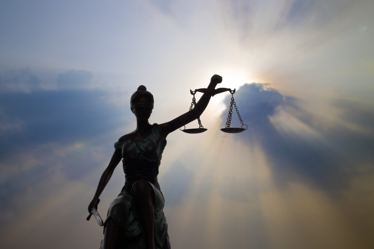 Statue de la justice tenant une balance déséquilibrée, éclairée par une lumière céleste perçant les nuages - une image symbolique illustrant la nécessité d’équité dans la gestion d’un conflit au travail. Lorsqu’un déséquilibre perçu s’installe entre les droits, les devoirs ou la reconnaissance des parties, le conflit peut s’intensifier. La justice, ici aveugle mais éclairée, rappelle l'importance d’une médiation impartiale pour restaurer la confiance et l’équilibre relationnel en entreprise.