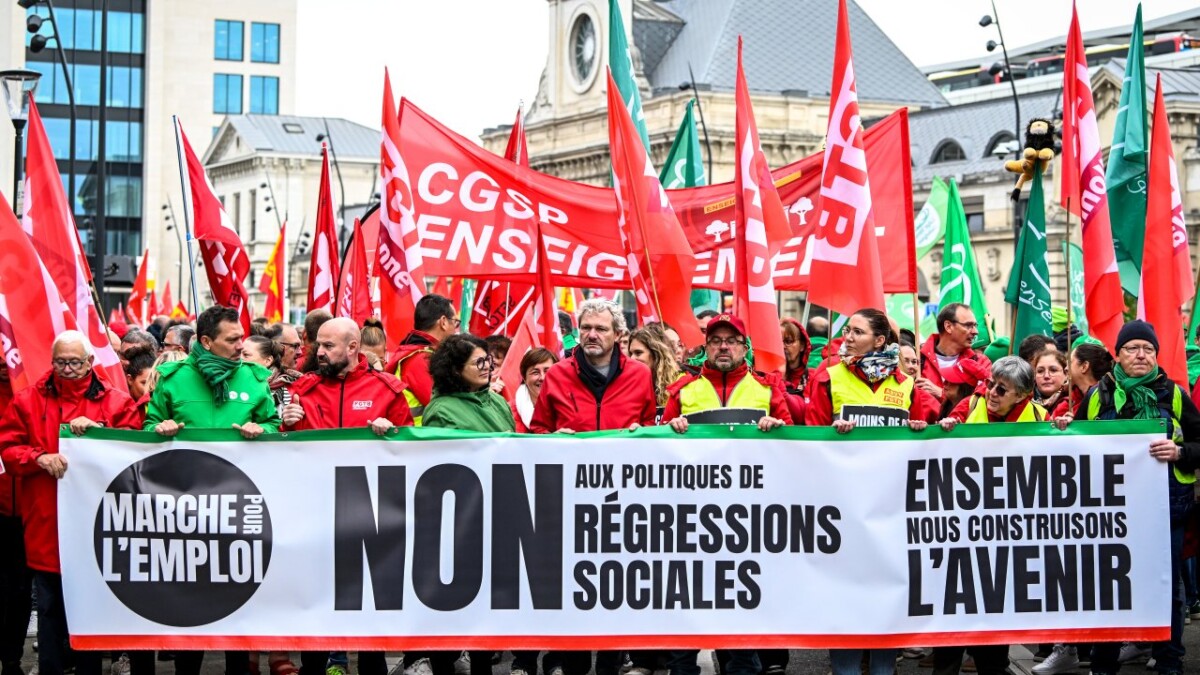 Des manifestants défilent dans une grande ville belge lors d’une grève nationale, portant des drapeaux rouges et verts représentant différentes organisations syndicales. Au premier plan, une large banderole proclame « NON aux politiques de régressions sociales – Ensemble, nous construisons l’avenir ». Cette image symbolise l’unité syndicale et la mobilisation collective autour des enjeux sociaux et économiques. Elle illustre l’article sur la grève du 14 octobre 2025 en Belgique, présentée comme un révélateur du climat social et du dialogue entre employeurs, travailleurs et délégués syndicaux.