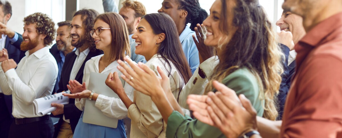 L’image montre un groupe de professionnels, hommes et femmes de différentes origines, en train d’applaudir avec enthousiasme. Leurs expressions sont joyeuses, souriantes, et traduisent une atmosphère de cohésion, de reconnaissance mutuelle et de réussite collective. Ils semblent réagir à une prise de parole, une annonce ou un résultat positif lors d’une réunion ou d’un événement interne à l’entreprise. Cette image illustre de manière visuelle les bénéfices concrets d’un dialogue social constructif, où la collaboration avec les délégués syndicaux est bien gérée. Elle reflète l’impact d’un climat social apaisé, d’une communication fluide et d’une relation de confiance entre les acteurs de l’entreprise. Elle symbolise une organisation où chacun, y compris le délégué syndical, a un rôle reconnu et valorisé dans la réussite commune.
