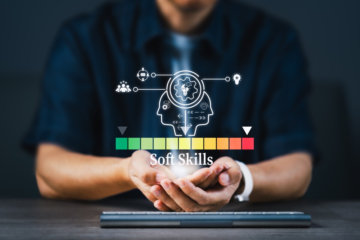 L’image montre un individu assis à un bureau, les mains ouvertes comme pour soutenir ou présenter quelque chose. Au-dessus de ses paumes, un graphique lumineux en réalité augmentée symbolise le concept de « Soft Skills ». On y voit deux profils humains stylisés en surimpression, reliés à des icônes représentant la communication, la créativité, l’intelligence émotionnelle, la collaboration et la résolution de problèmes. En dessous, une échelle de couleur allant du vert au rouge visualise le niveau ou l’intensité des compétences comportementales. Cette illustration évoque l'importance stratégique du développement des compétences humaines – en particulier chez les managers – pour la gestion proactive du conflit en entreprise. Elle souligne visuellement que les soft skills ne sont pas accessoires, mais bien au cœur de la capacité des leaders à détecter, désamorcer et transformer les tensions au travail.