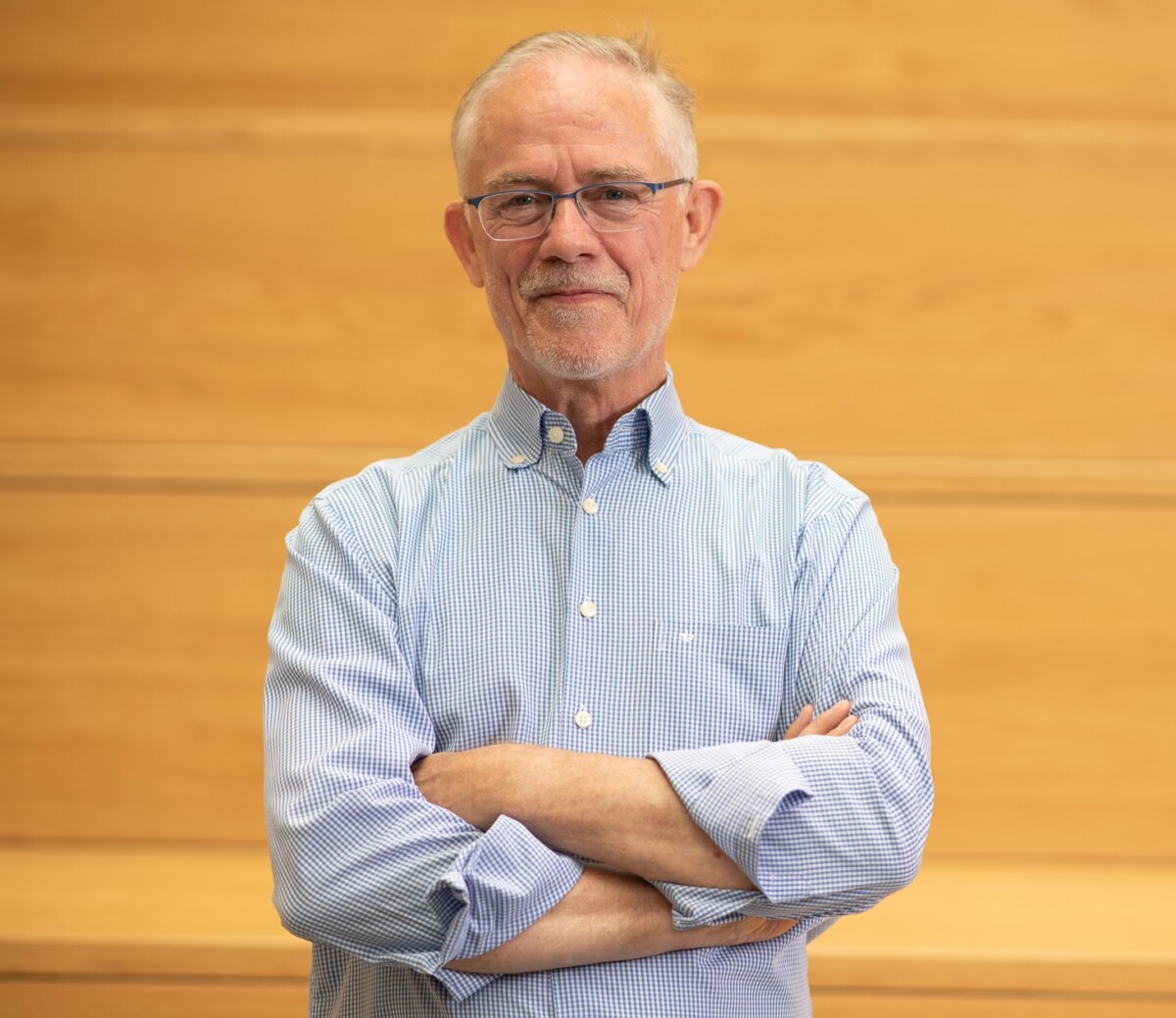 Portrait de Patrick Namotte, expert en dialogue social, bras croisés, regard calme et affirmé. Il se tient devant un fond en bois clair, évoquant la rigueur et la chaleur humaine. Cette image illustre la posture d’un médiateur expérimenté, à la fois accessible et solide, engagé dans la régulation des tensions sociales, la gestion des conflits collectifs et l'accompagnement des entreprises belges dans la reconstruction d’un dialogue social sain et durable.