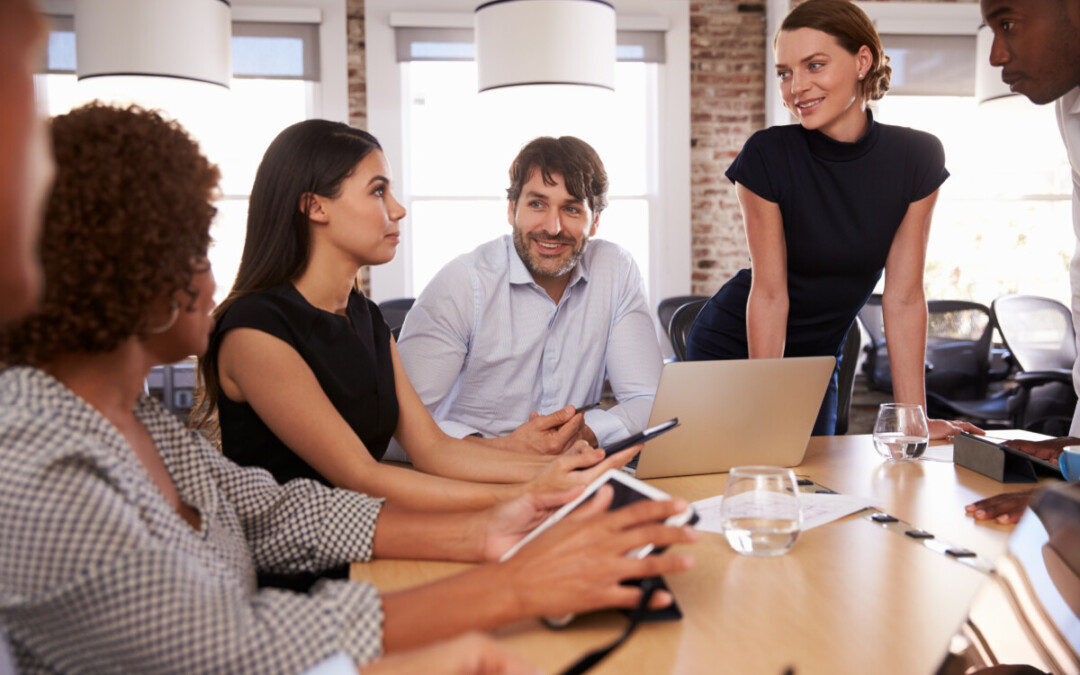 Réunion professionnelle dans un environnement de bureau moderne, cinq collègues – hommes et femmes issus de divers horizons – échangent de façon attentive et collaborative autour d’une table, incarnant la communication constructive et la gestion positive du conflit en entreprise.