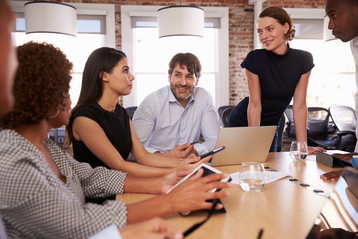 Réunion professionnelle dans un environnement de bureau moderne, cinq collègues – hommes et femmes issus de divers horizons – échangent de façon attentive et collaborative autour d’une table, incarnant la communication constructive et la gestion positive du conflit en entreprise.